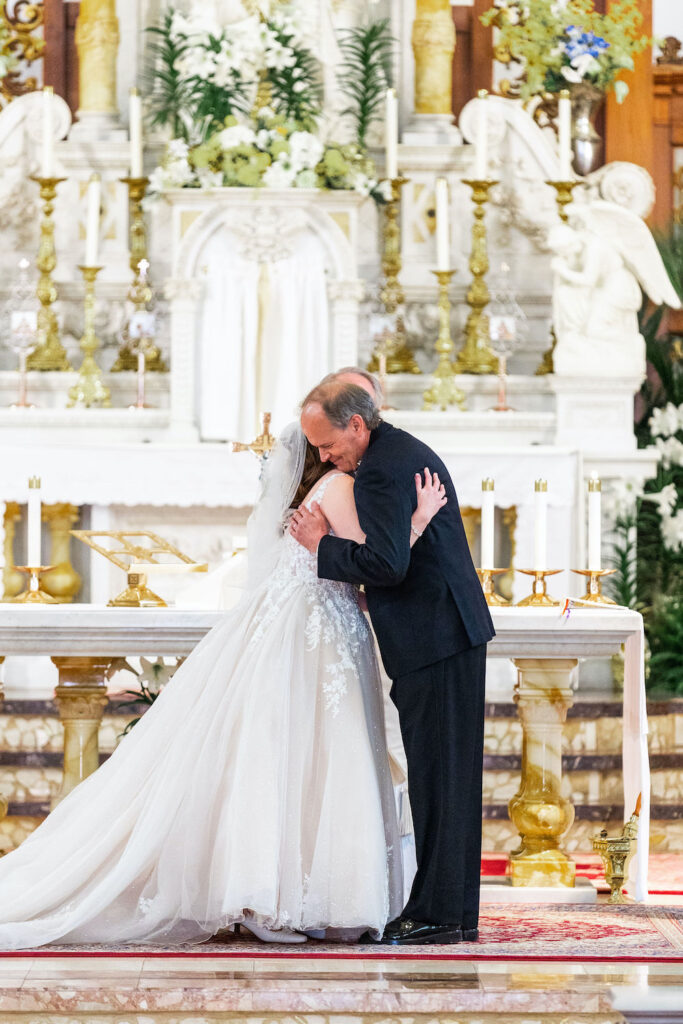 A bride in a white, lace-embellished gown and veil embraces a man in a dark suit