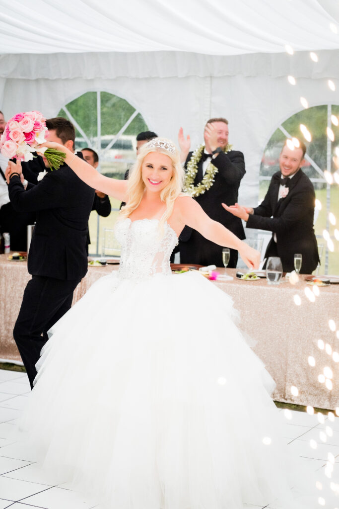 A joyful bride in a white gown and tiara dances, holding a bouquet of pink and white roses