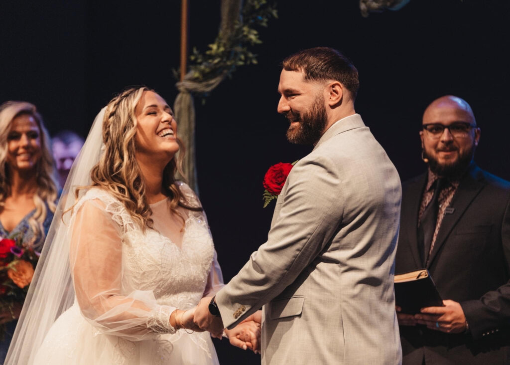 A bride and groom are joyfully holding hands during their wedding ceremony