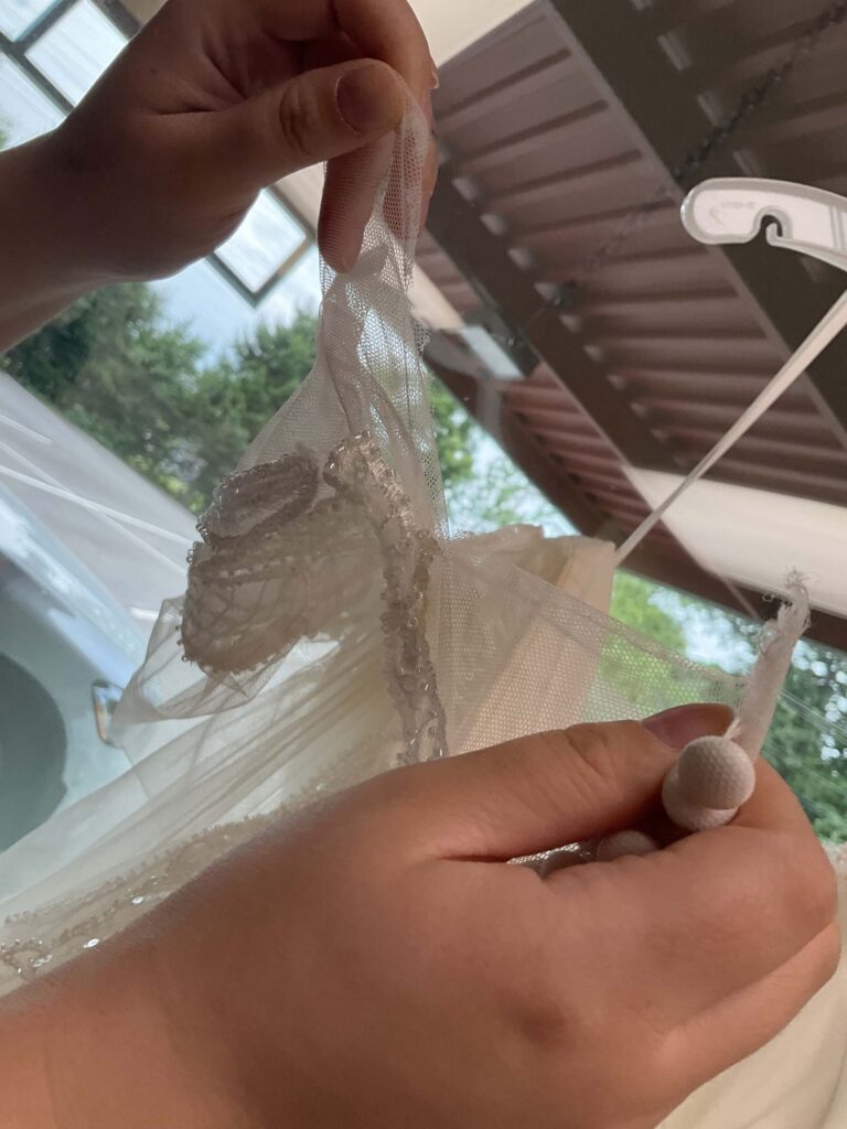 Hands are delicately holding a piece of sheer, beaded fabric from a garment