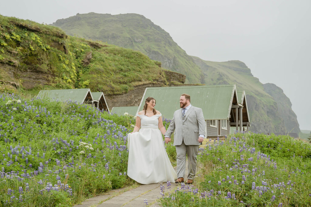 A couple in wedding attire walks hand in hand along a deserted black sand beach