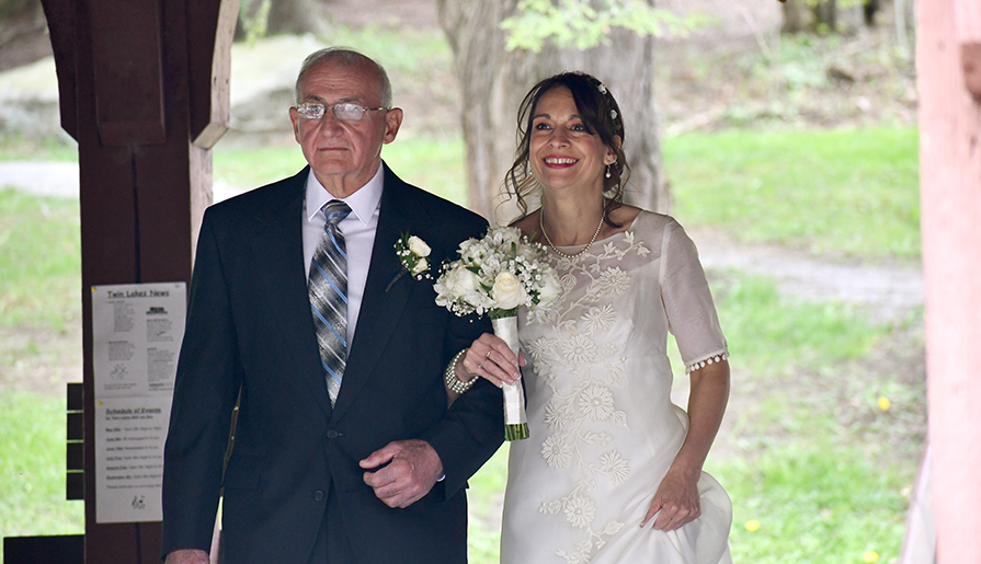 A bride in an elegant white dress adorned with floral embroidery holds a bouquet of white flowers