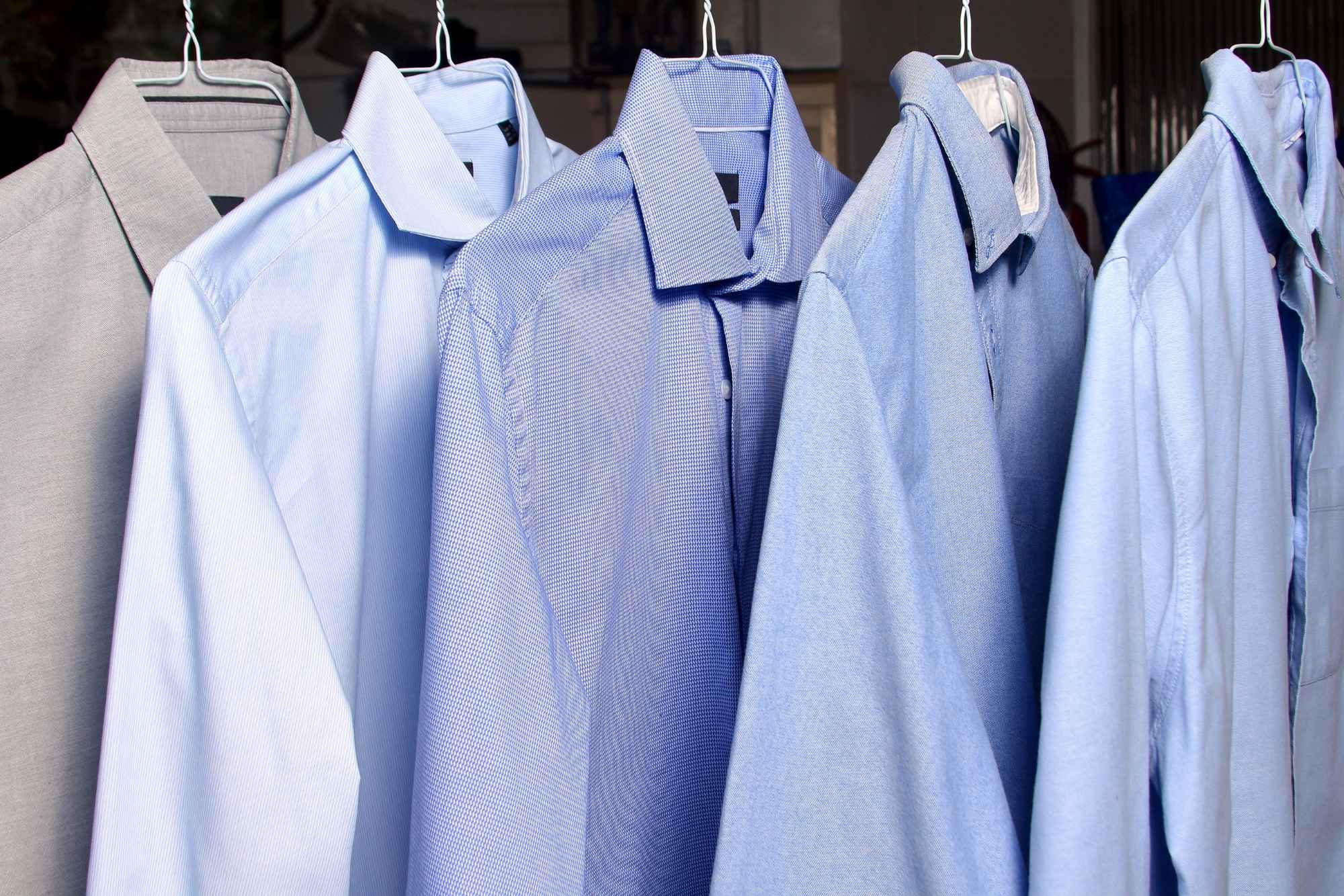 Five light blue and grey mens dress shirts on hangers