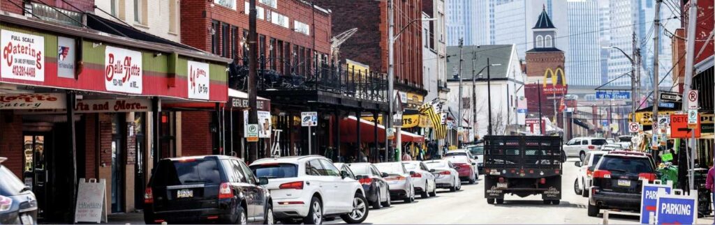 Busy urban street lined with parked cars and colorful storefronts