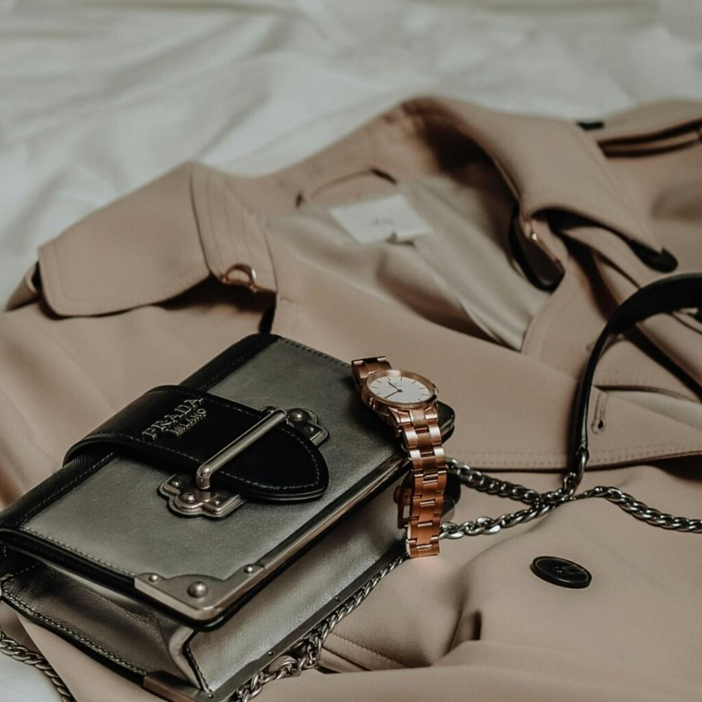 Image of a designer purse, coat, and watch laid out on a bedspread.